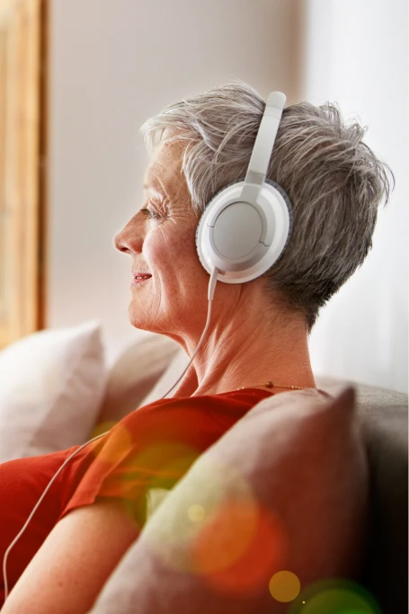 aeltere Frau mit Kopfhörern schaut aus dem Fenster und sitzt auf dem Sofa