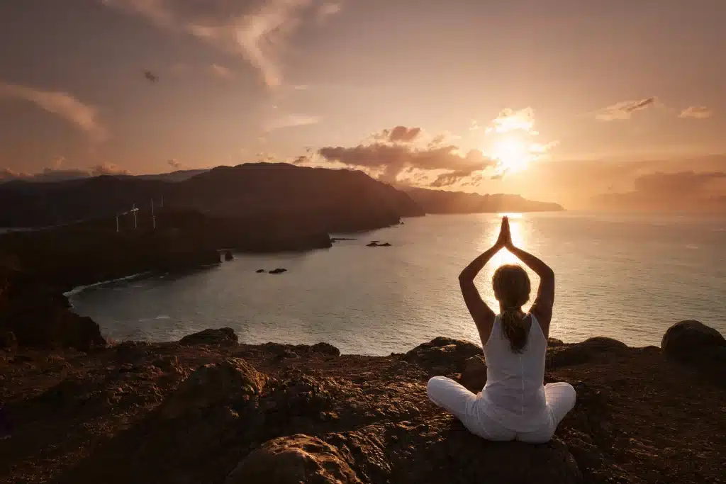 Frau in Yoga-Position vor einem See im Sonnenuntergang