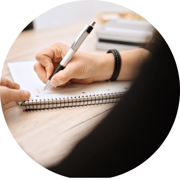 Hand von Kundenbetreuerin von Balance First schreibt Stressmanagementplaene auf einen Block mit einem Stift